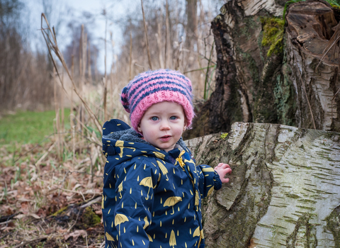 Poppy the toddler stands next to a tree stump